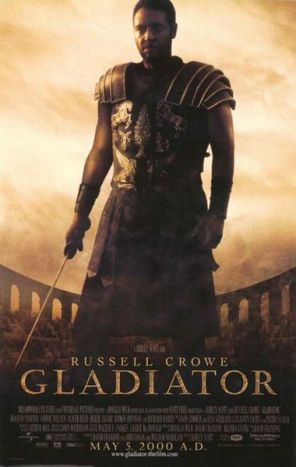A man standing at the center of the image is wearing armor and is holding a sword in his right hand. In the background is the top of the Colosseum with a barely visible crowd standing in it. The poster includes the film's title, cast credits and release date. Gladiator