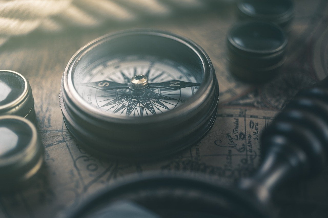 An antique compass and map symbolise magical pursuit and the direction revealed by Locate Creature
